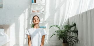beautiful happy woman with closed eyes practicing yoga in lotus position in bedroom in the morning