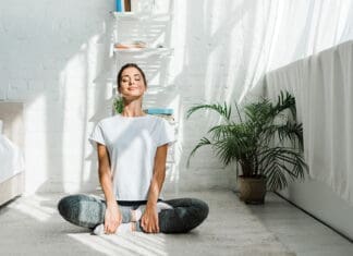 beautiful happy woman with closed eyes practicing yoga in lotus position in bedroom in the morning