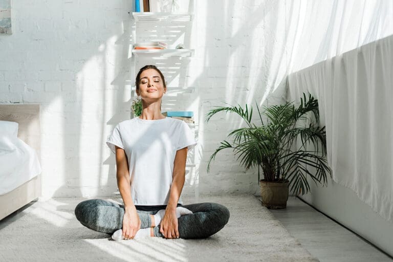 beautiful happy woman with closed eyes practicing yoga in lotus position in bedroom in the morning