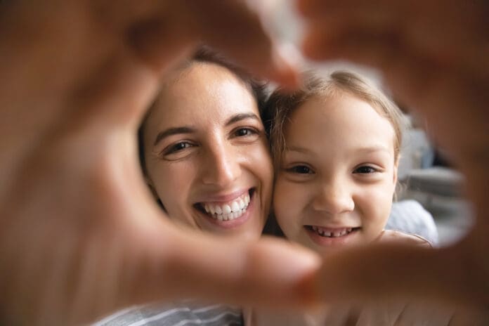 Smiling Hispanic mom and biracial daughter show heart sign