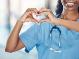 Closeup african american woman nurse making a heart shape with her hands while smiling and standing in hospital. Take care of your heart and love your body. Health and safety in the field of medicine
