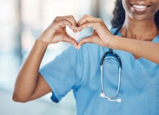 Closeup african american woman nurse making a heart shape with her hands while smiling and standing in hospital. Take care of your heart and love your body. Health and safety in the field of medicine