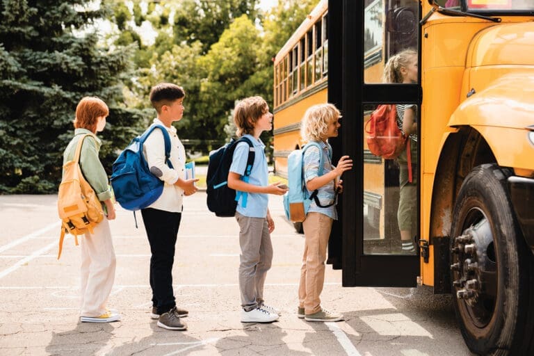 Multiethnic mixed-race pupils classmates schoolchildren students standing in line waiting for boarding school bus before starting new educational semester year after summer holidays