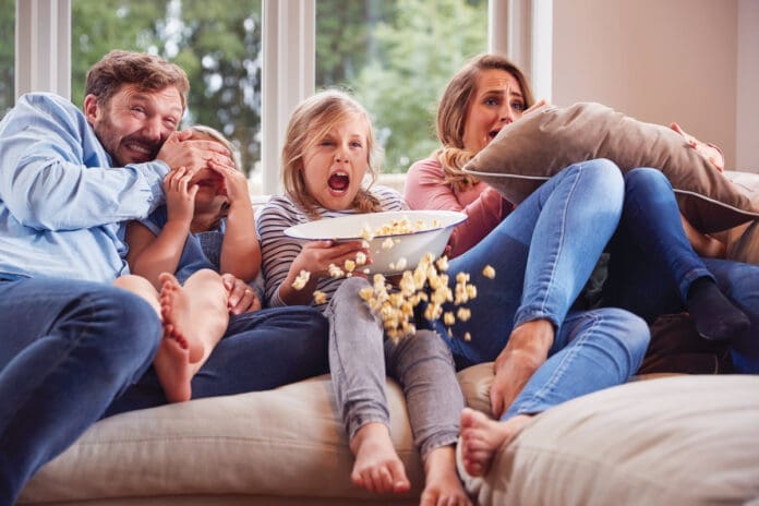 Frightened Family Sitting On Sofa At Home Watching Horror Movie On TV With Popcorn Frightened Family Sitting On Sofa At Home Watching Horror Movie On TV With Popcorn