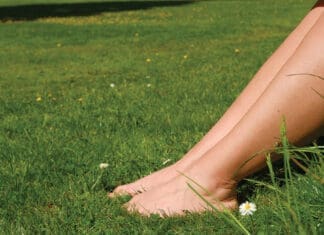 Grounding – Why Should You Be Doing It? Women's feet on a green lawn in the park. Relaxation, Rest. Grounding. Woman resting on lawn.