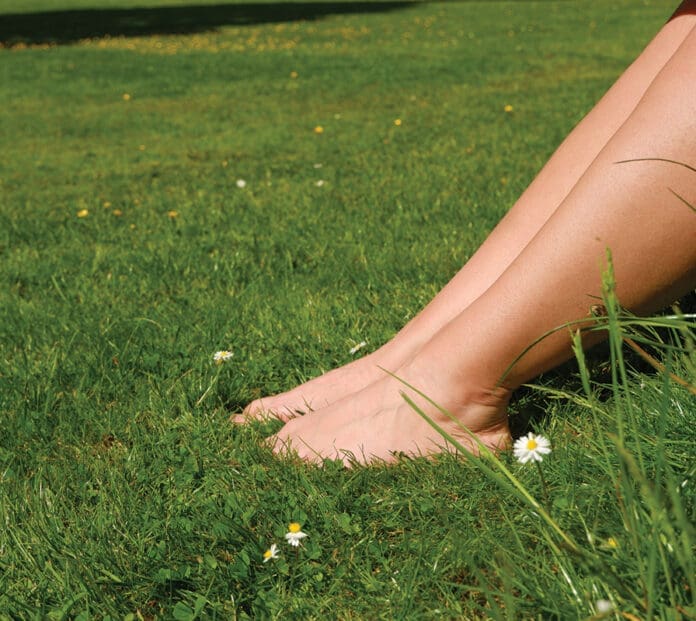 Women's feet on a green lawn in the park. Relaxation, Rest. Grounding. Woman resting on lawn.