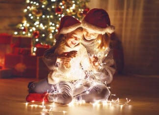 Merry Christmas! mother and child daughter with a glowing Christmas garland near tree