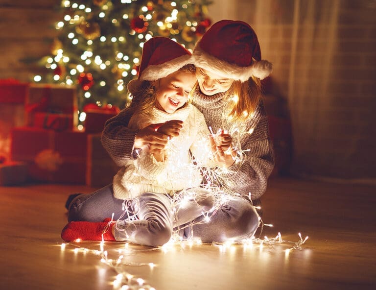 Merry Christmas! mother and child daughter with a glowing Christmas garland near tree