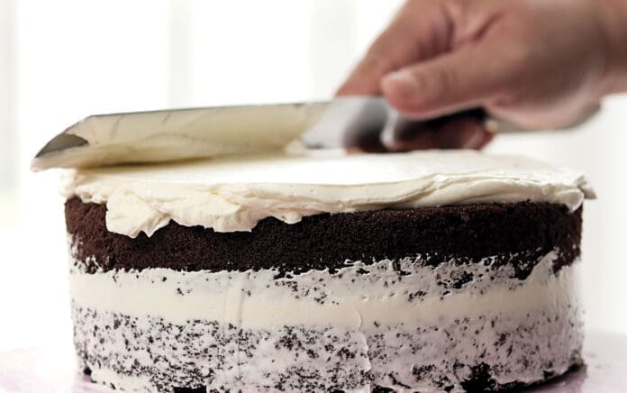 Spreading white butter cream on homemade chocolate cake.