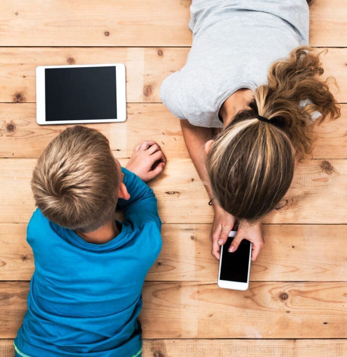 Top view image of two kids lying on the floor and playing with tablet and smartphone watching movie or gaming.
