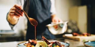 Chef pouring special sauce on pork ribs in the kitchen