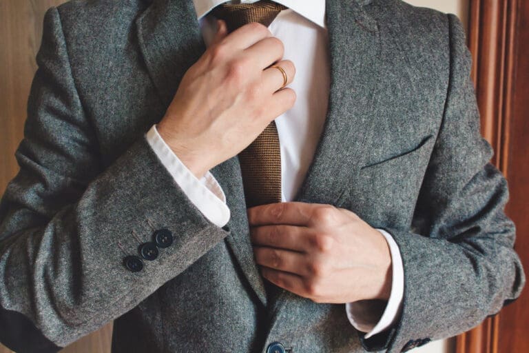 Man in smart suit wearing wedding ring adjusting tie. Elegant tailor-made clothing.