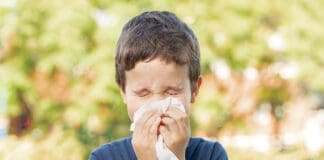 Allergic child sneezing covering nose with wipe in a park in spring or summer season