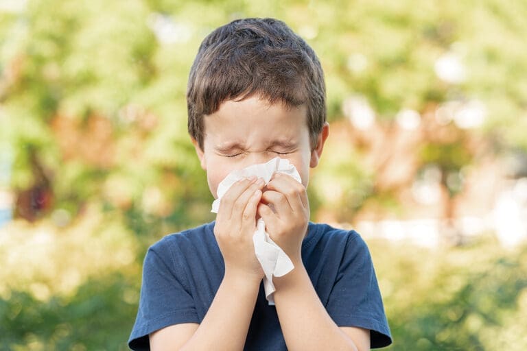 Allergic child sneezing covering nose with wipe in a park in spring or summer season