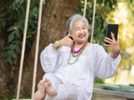 Elderly Woman Relaxing on a Swing While Using a Tablet in a Serene Outdoor Setting, Surrounded by Lush Greenery and Natural Beauty