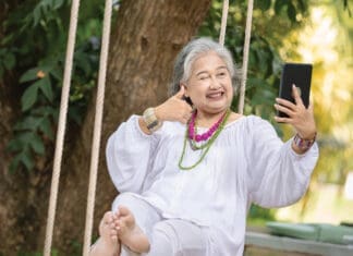 Elderly Woman Relaxing on a Swing While Using a Tablet in a Serene Outdoor Setting, Surrounded by Lush Greenery and Natural Beauty