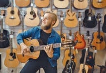 Young man plays on acoustic guitar in music store. Assortment in musical instruments shop, male musician buying equipment