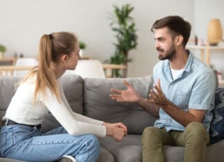 Serious young couple sitting together on sofa, talking about relationships, spending time together at home, focused wife listening to speaking husband, friends having conversation